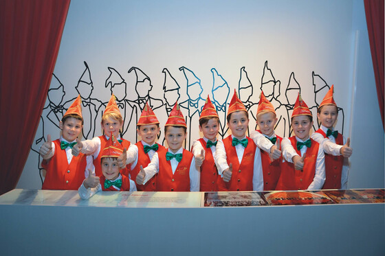 Eine Gruppe von Kindern in roten Anzügen und Hüten posiert fröhlich für die Kamera.