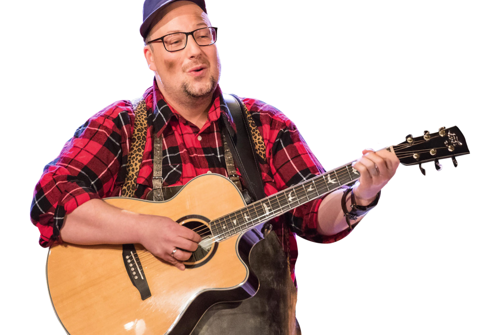 Ein Musiker mit Gitarre singt fröhlich in einem karierten Hemd. | © DerSchmied