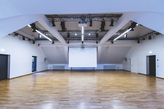 Großer, heller Veranstaltungsraum mit Holzfußboden und Projektionsleinwand.