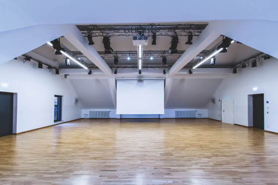 Großer, heller Veranstaltungsraum mit Holzfußboden und Projektionsleinwand.