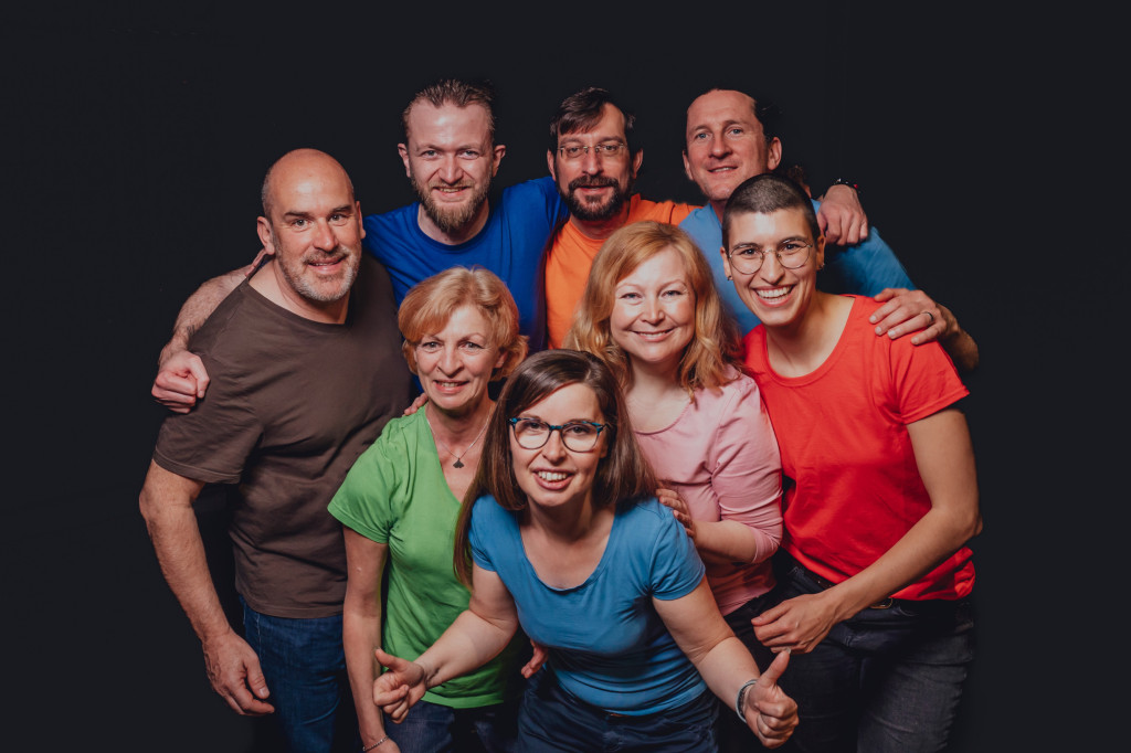 Eine Gruppe von acht Personen lächelt fröhlich im Improtheater.