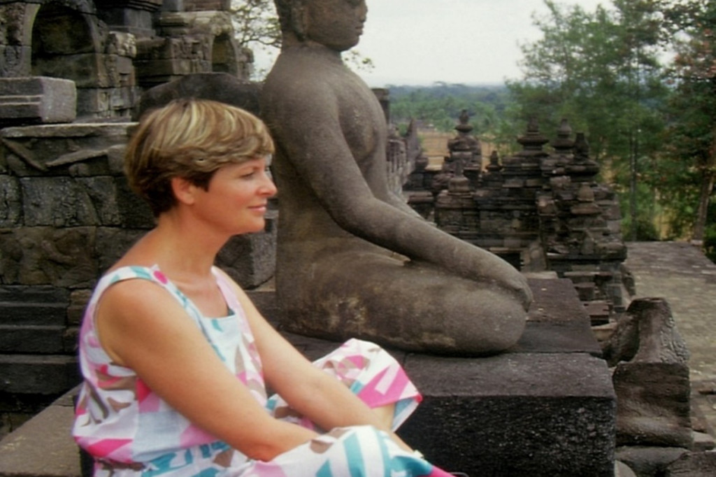 Eine Frau sitzt entspannt neben einer Buddha-Statue in Borobudur. | © Klapheck